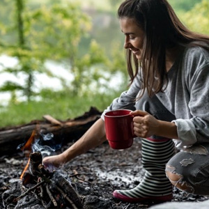 Woman next to campfire holding a custom promotional mug